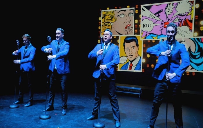 A group of men in blue suits singing on stage.